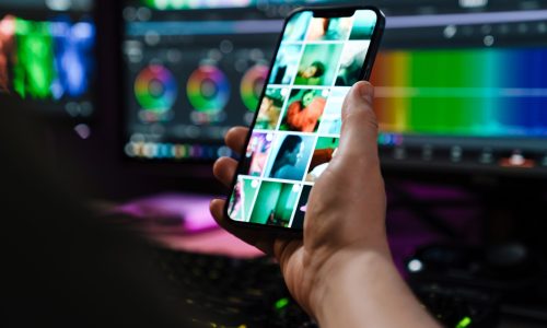 Close up of a white man hand holding mobile phone over computer screen on a table indoors