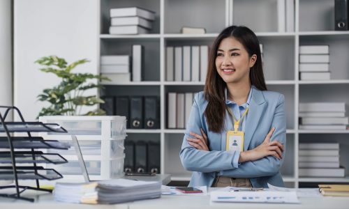 Attractive asian businesswoman standing with crossed arms and looking at camera in office confident and happy with business success..