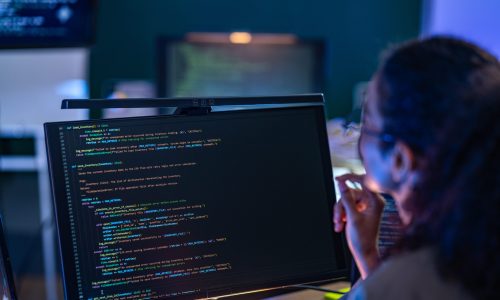 Focused Brazilian AI programmer analyzing complex source code and real time data logs on high resolution displays in a tech hub.