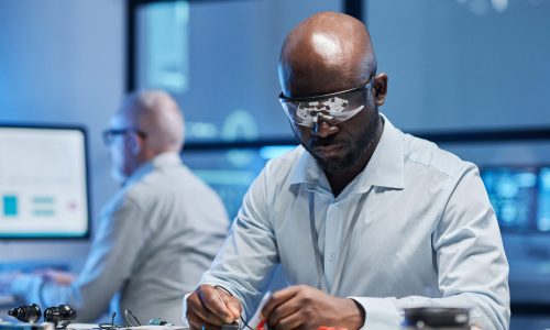 African American engineer in protective glasses working with computer board at table in the lab