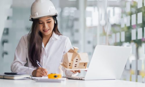 Female architect designer in an office working on a laptop is modeling a house and writing a housing project.