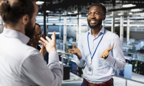 Smiling diverse engineering team reviewing performance dashboards with AI tools for server rigs. Server room workers overseeing machine learning algorithms on platform workstation.